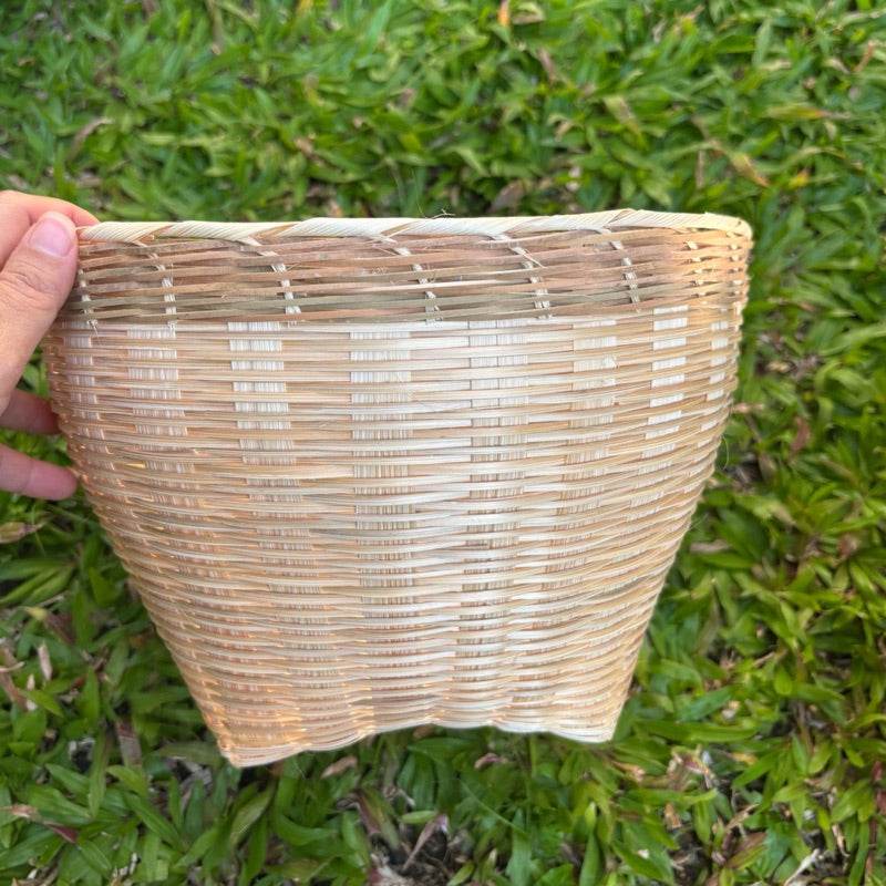 Hand holding a handmade Thai bamboo basket with natural woven texture against green grass background