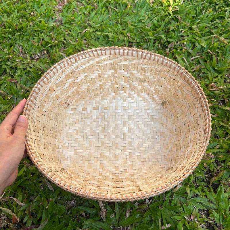 Hand holding a handmade Thai bamboo basket with natural woven texture on green grass