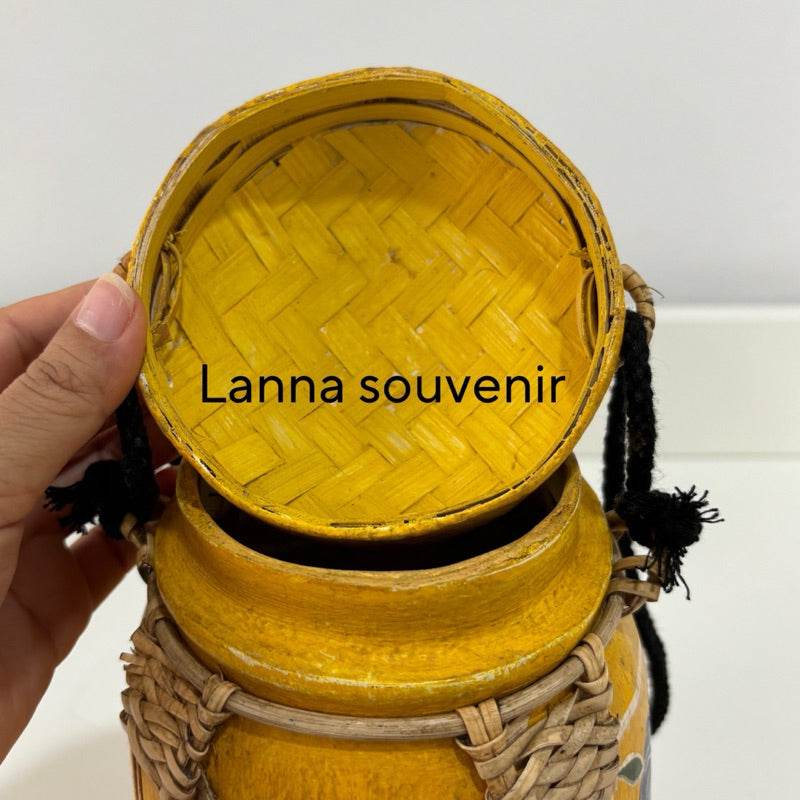 Handmade Thai bamboo rice box with woven lid and yellow finish held in hand
