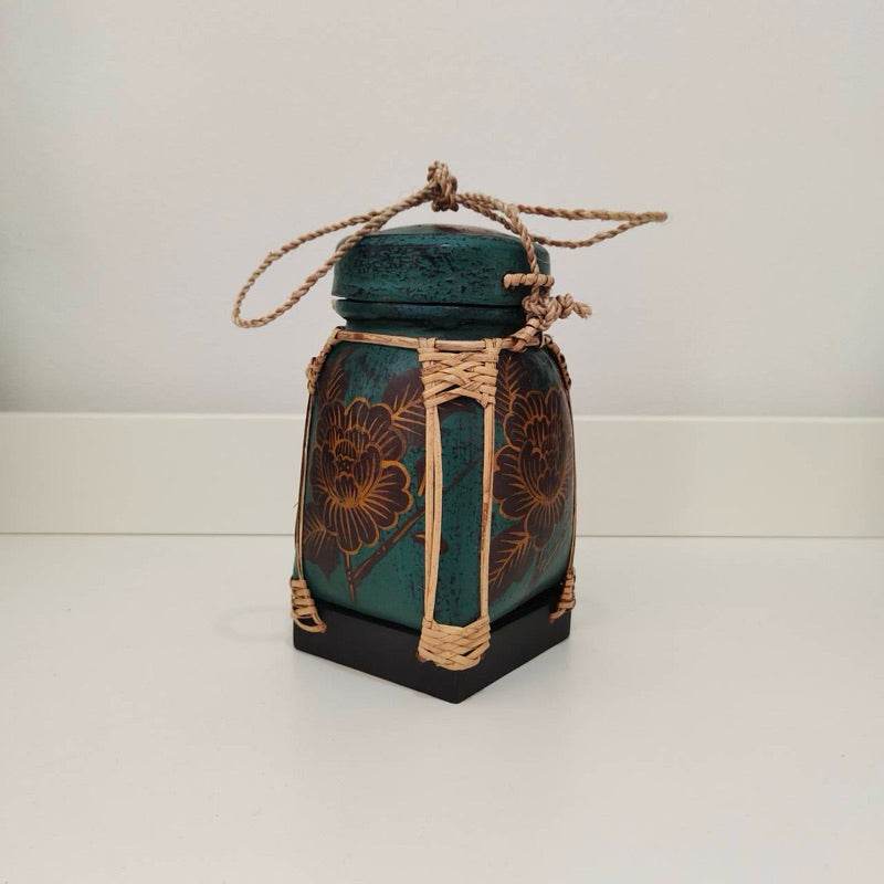 Handmade Thai bamboo rice box with floral design and rope detailing on green ceramic base