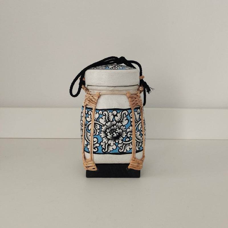 Handmade Thai bamboo rice box with intricate blue floral design and black carrying strap
