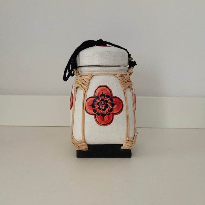 Handmade Thai bamboo rice box with red floral design and woven details on white background