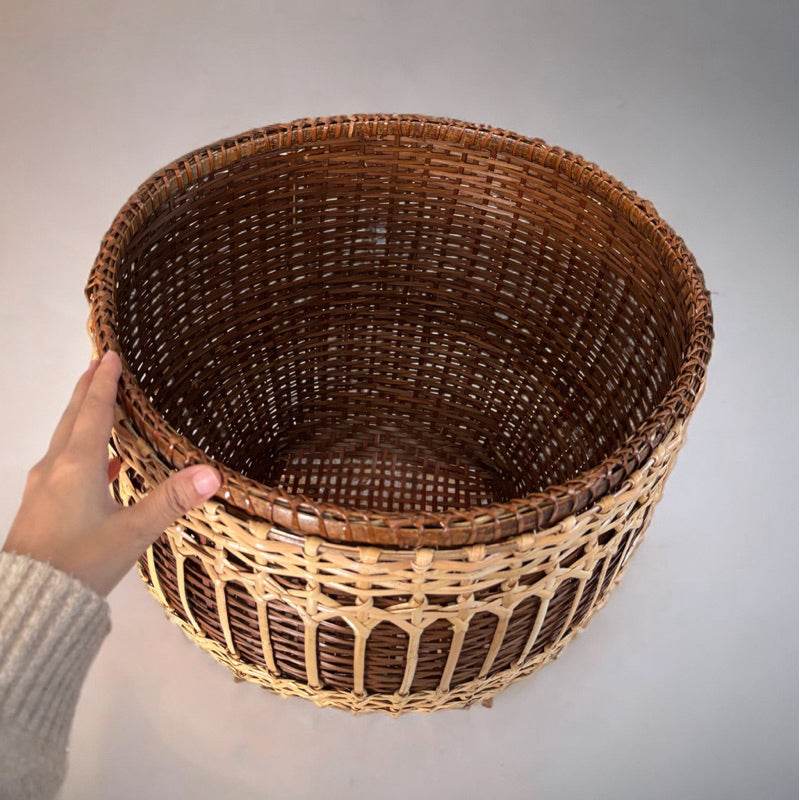 Hand holding empty handwoven bamboo rattan basket with light and dark brown natural fibers