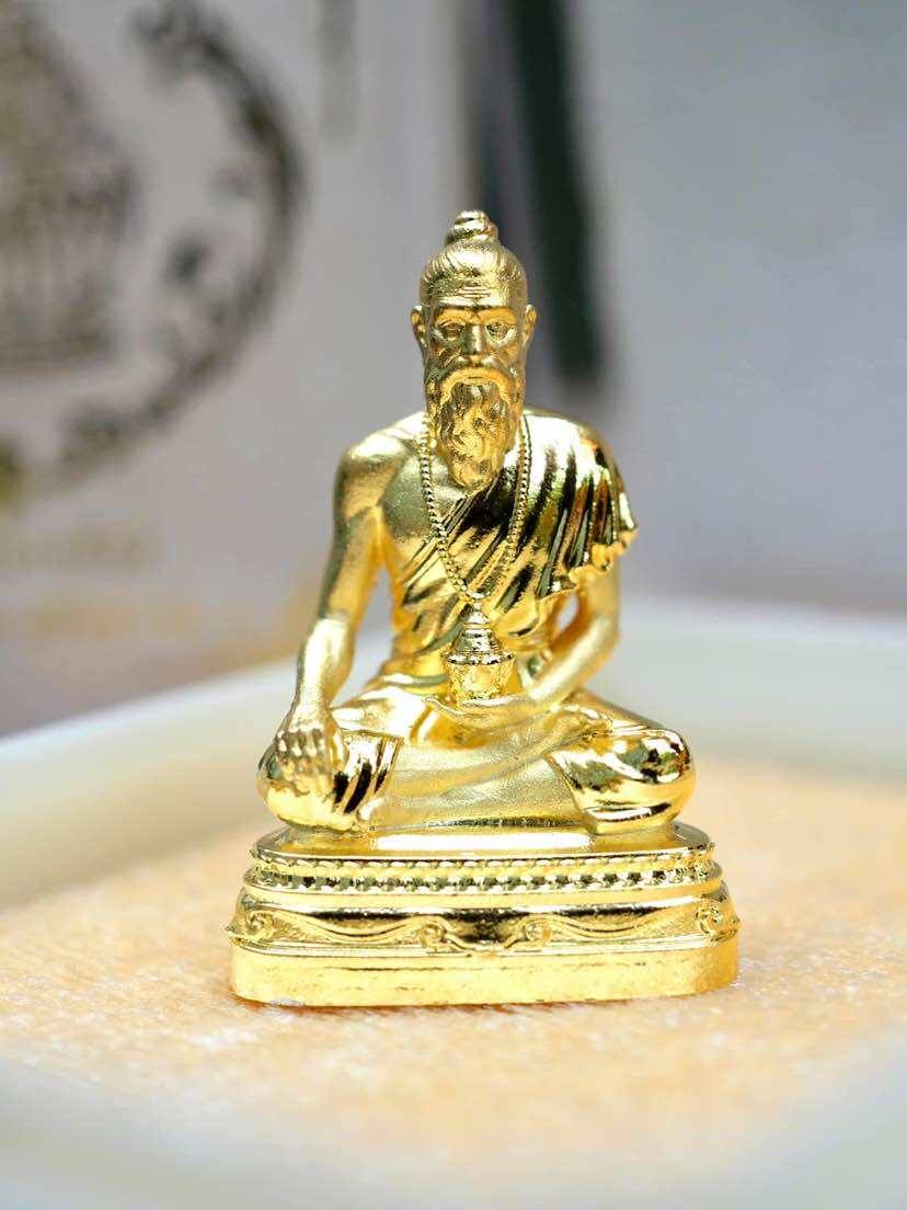Golden Jivaka Komarabhacca amulet for health sitting on a decorative base for spiritual well-being