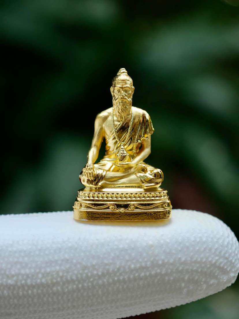 Golden Jivaka Komarabhacca amulet for health sitting on a finger, symbolizing wellness and strength