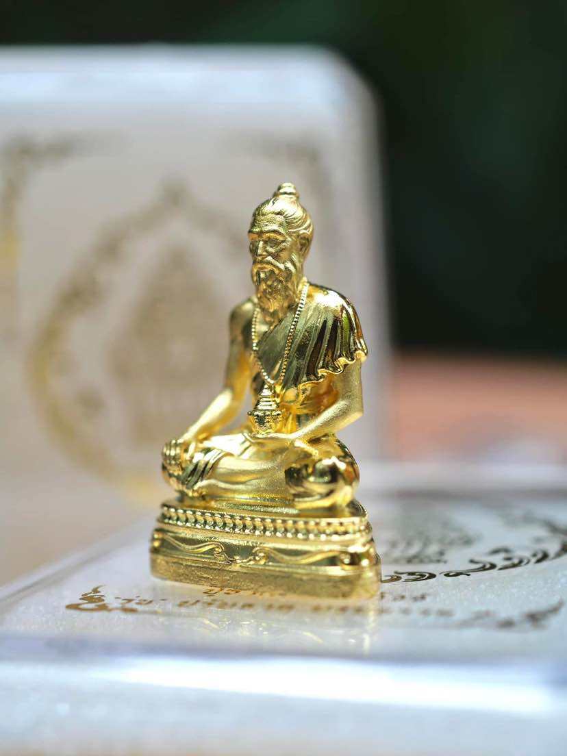 Gold Jivaka Komarabhacca amulet for health displayed elegantly on a decorative surface