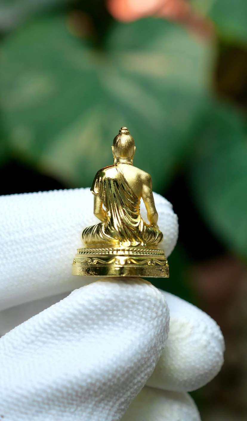 Gold Jivaka Komarabhacca amulet for health held in a gloved hand with a blurred background