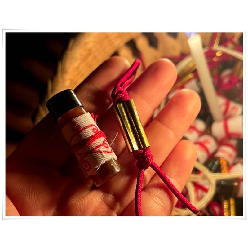 Khmer attraction oil for love and luck in a small vial held by hand with decorative string