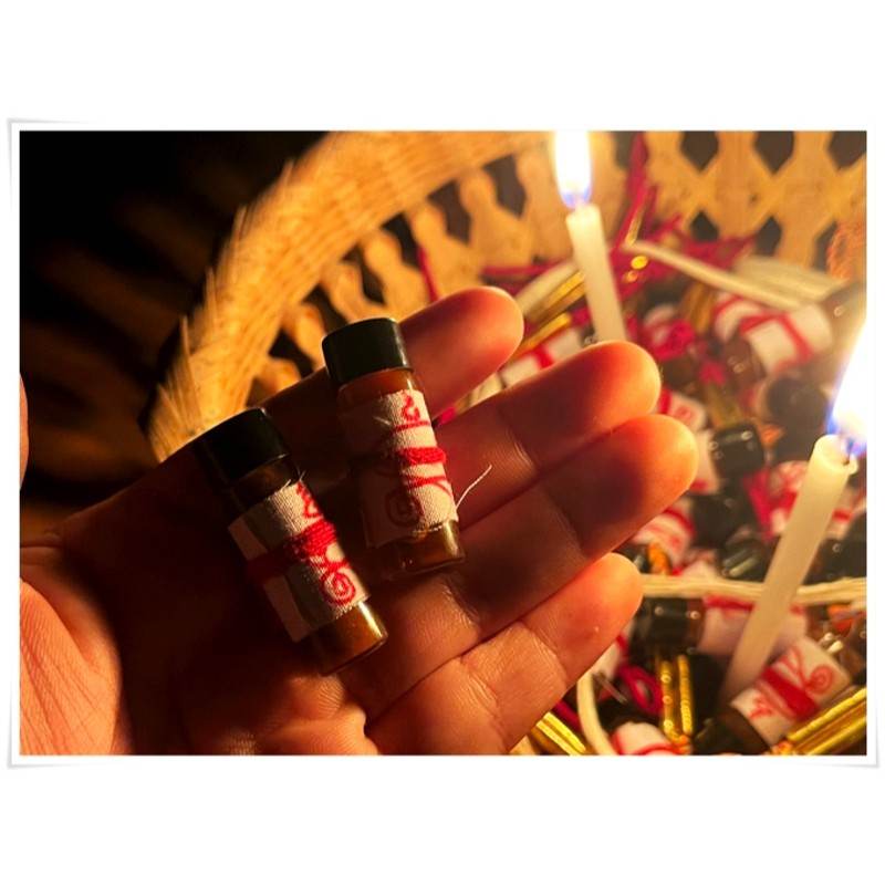 Two bottles of Khmer attraction oil for love and luck held in hand, surrounded by candles and ritual items