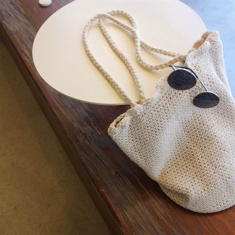 Korean style handwoven shoulder bag in cream color lying on wooden table with black sunglasses