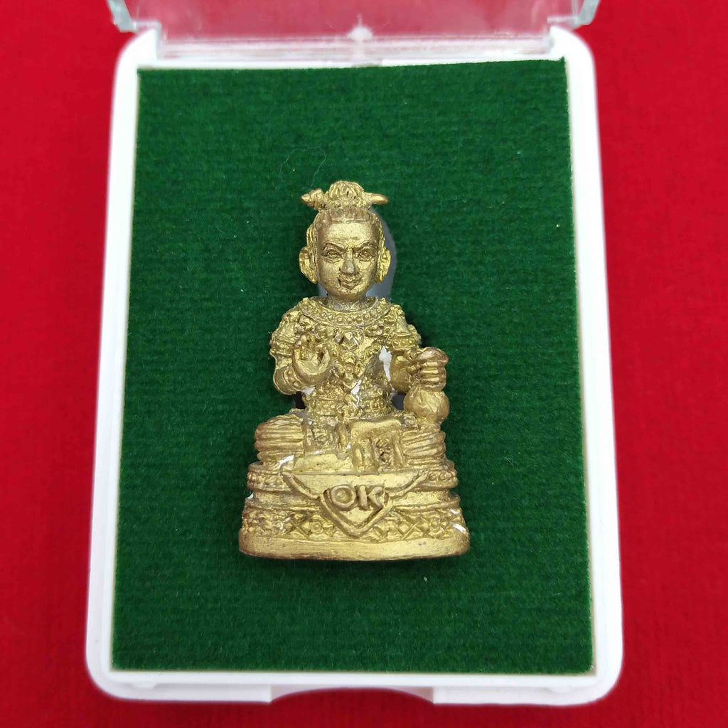 Kuman Thong amulet for prosperity displayed in a protective box with a green base and red background