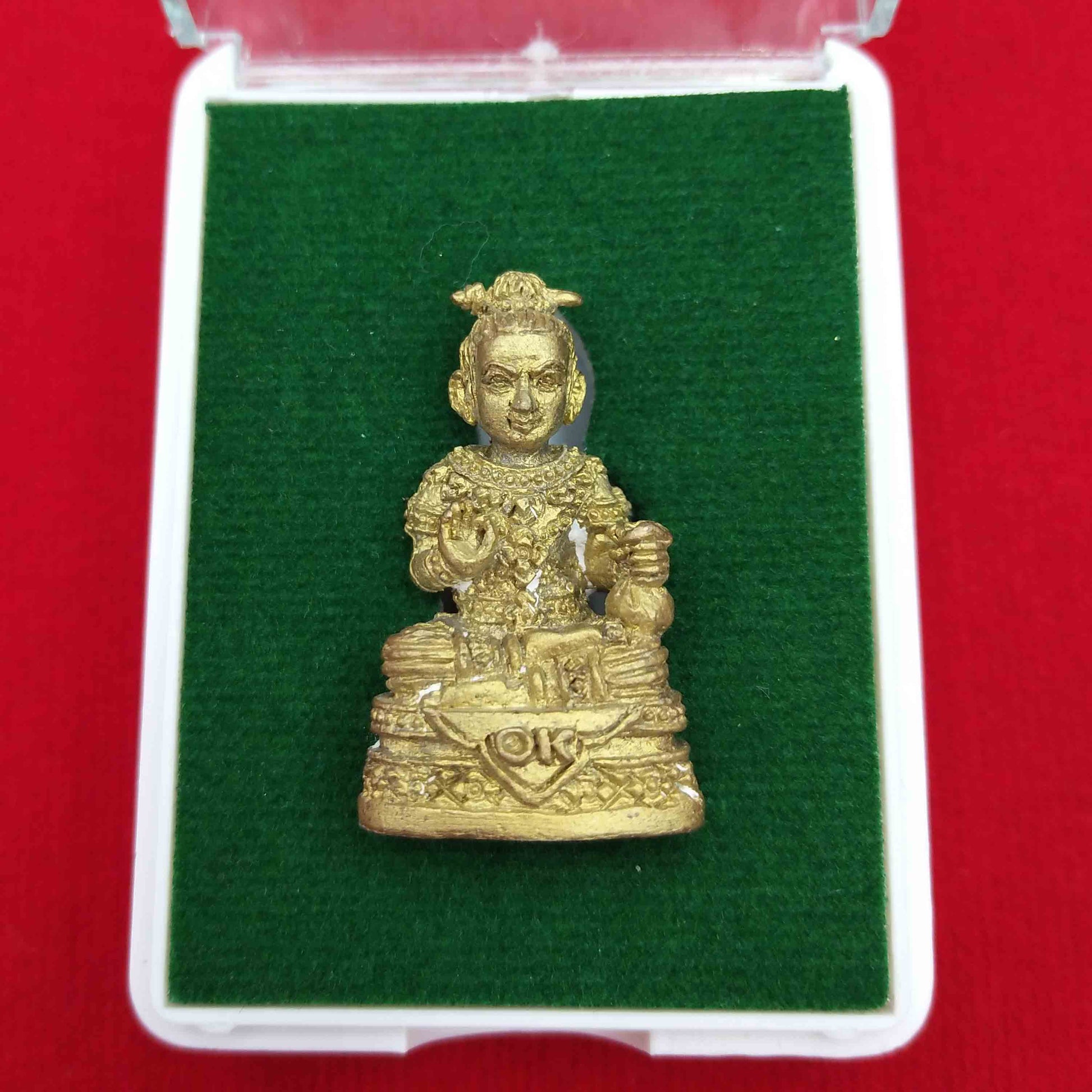 Kuman Thong amulet for prosperity displayed in a protective case with green base