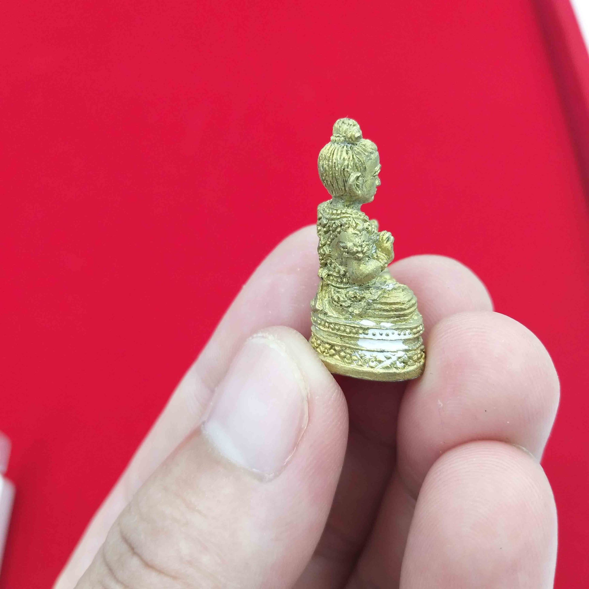 Handheld Kuman Thong amulet for prosperity displayed with intricate details in gold finish