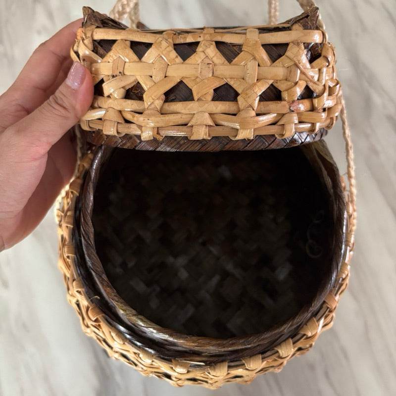 Hand holding open bamboo sticky rice box from Thailand with woven natural fibers and lid
