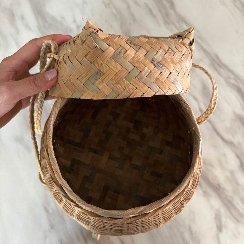 Hand holding the lid of a bamboo sticky rice box from Thailand with woven basket design
