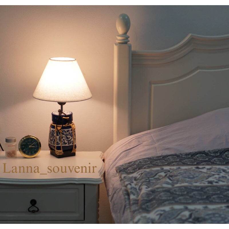 Handmade bamboo lamp for bedroom on a white bedside table next to a bed with patterned bedding