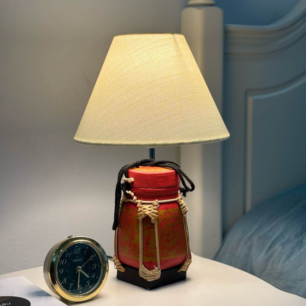 Handmade bamboo lamp for bedroom with red and black base and beige fabric lampshade on nightstand