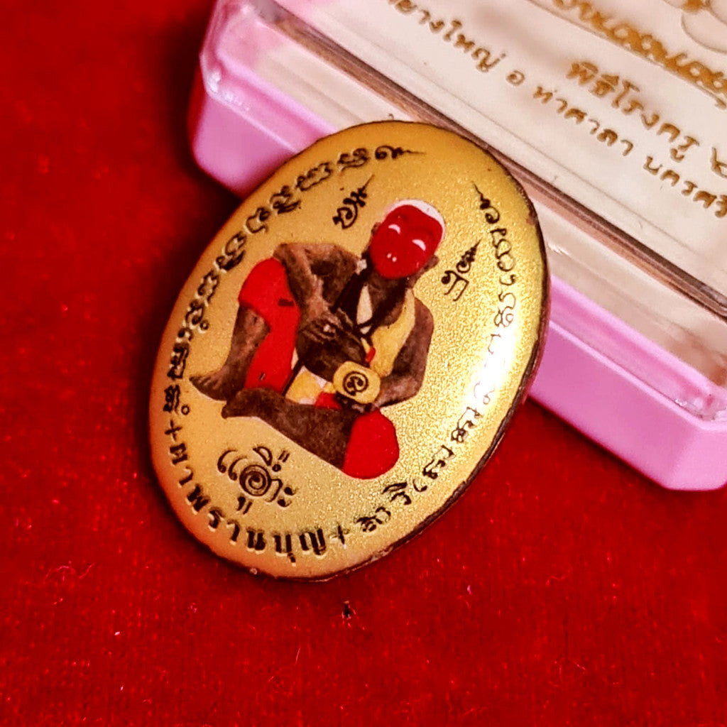 Locket Ta Pran Boon golden back with traditional Thai inscriptions and seated figure placed on red cloth