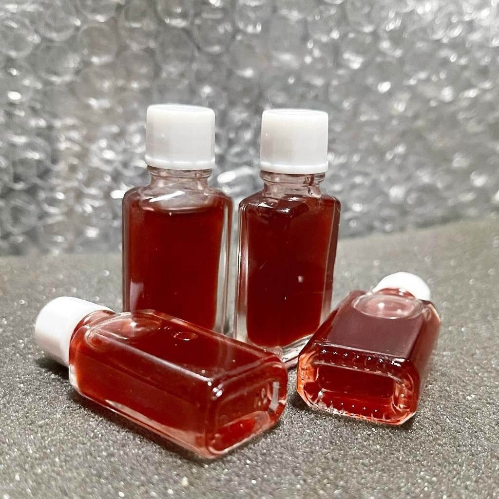 Four small glass bottles of red oil with white caps on gray surface Lohit Sawat oil for attraction