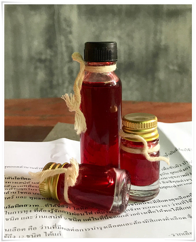 Three small glass bottles of red oil tied with twine on Thai script paper Lohit Sawat oil for attraction