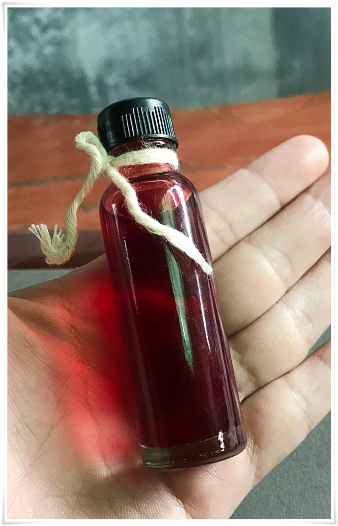 Small glass bottle of red oil with black cap and twine held in hand Lohit Sawat oil for attraction