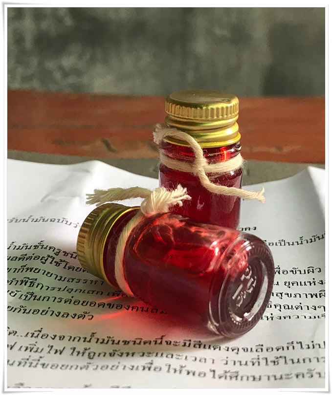 Two small glass bottles of red oil with gold caps and twine on Thai script paper Lohit Sawat oil for attraction by Thai Blessing