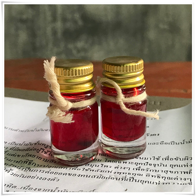 Two small glass vials of red oil with gold caps and twine on Thai script paper Lohit Sawat oil for attraction