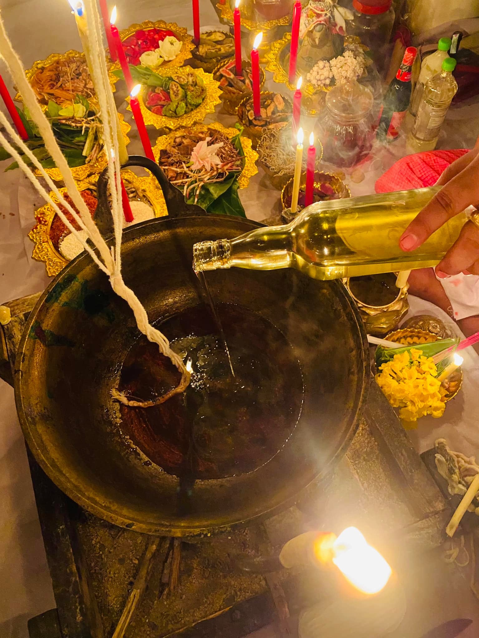 Lohit Sawat oil for attraction being poured into ceremonial cauldron during Thai blessing ritual with candles and offerings