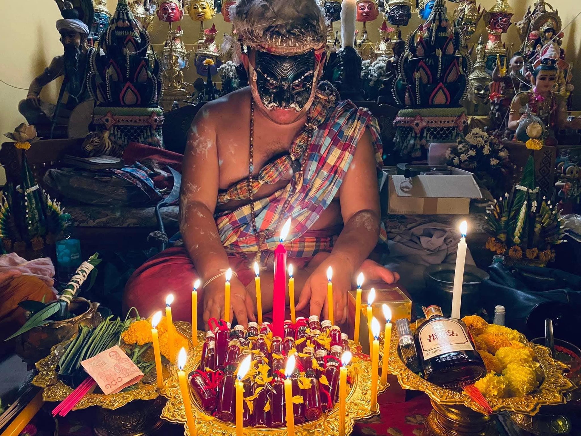 Thai ritual altar with candles, marigolds, small bottles of Lohit Sawat oil for attraction and offerings