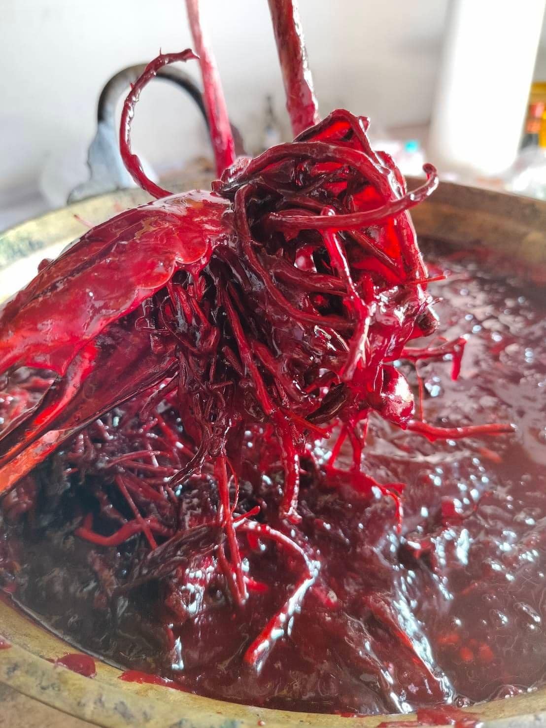 Thai Blessing Co brass bowl of deep red oil with shredded herbs being stirred Lohit Sawat oil for attraction