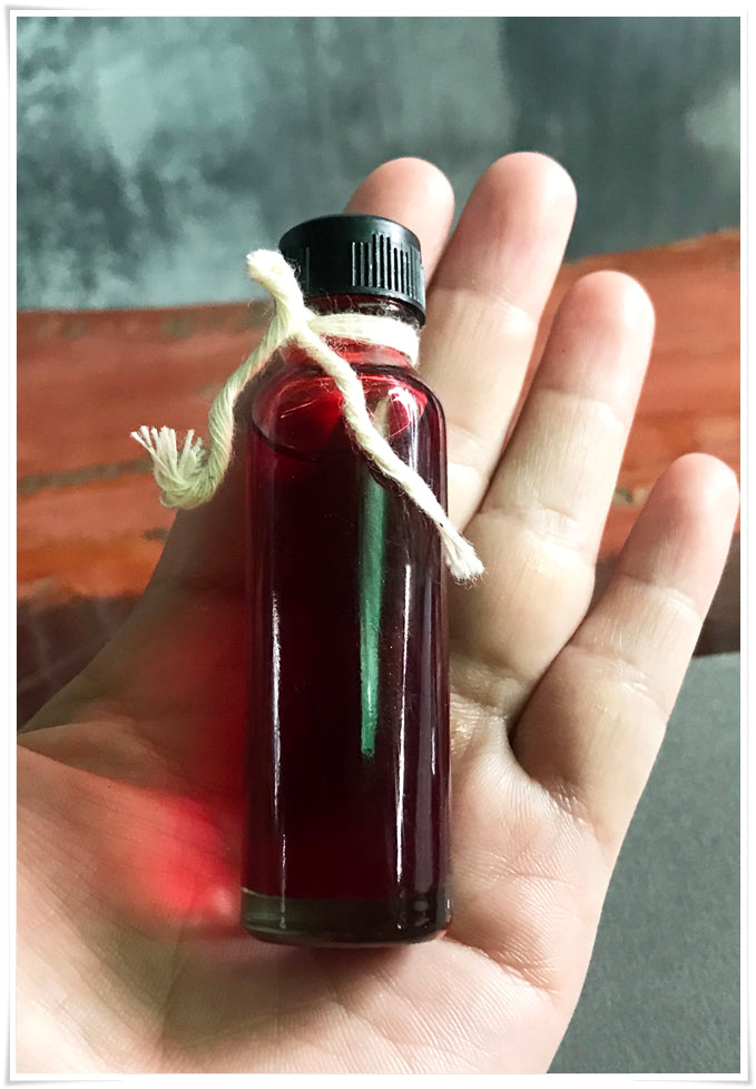 Small glass bottle of red oil in hand with twine around cap Thai Blessing Co Lohit Sawat oil for attraction