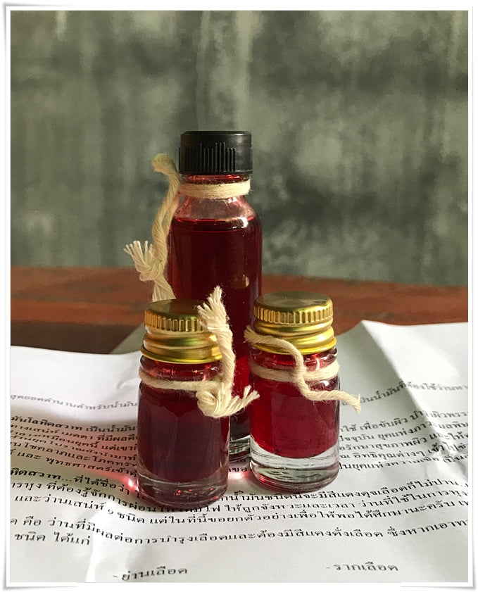 Three small glass bottles of red oil on paper with twine and gold lids, Lohit Sawat oil for attraction by Thai Blessing Co