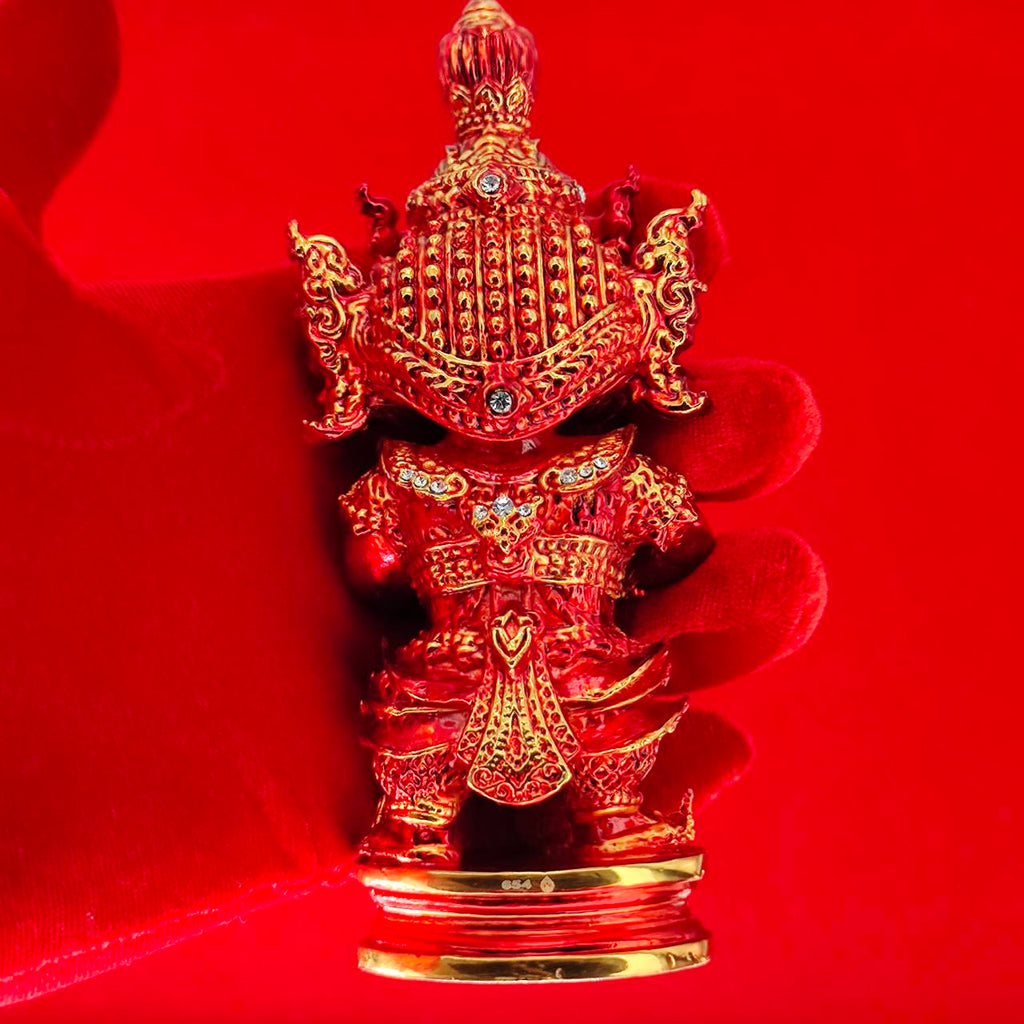 Lord Vesuvanna lucky charm figurine in detailed red design with gold accents, held by a gloved hand against a red background