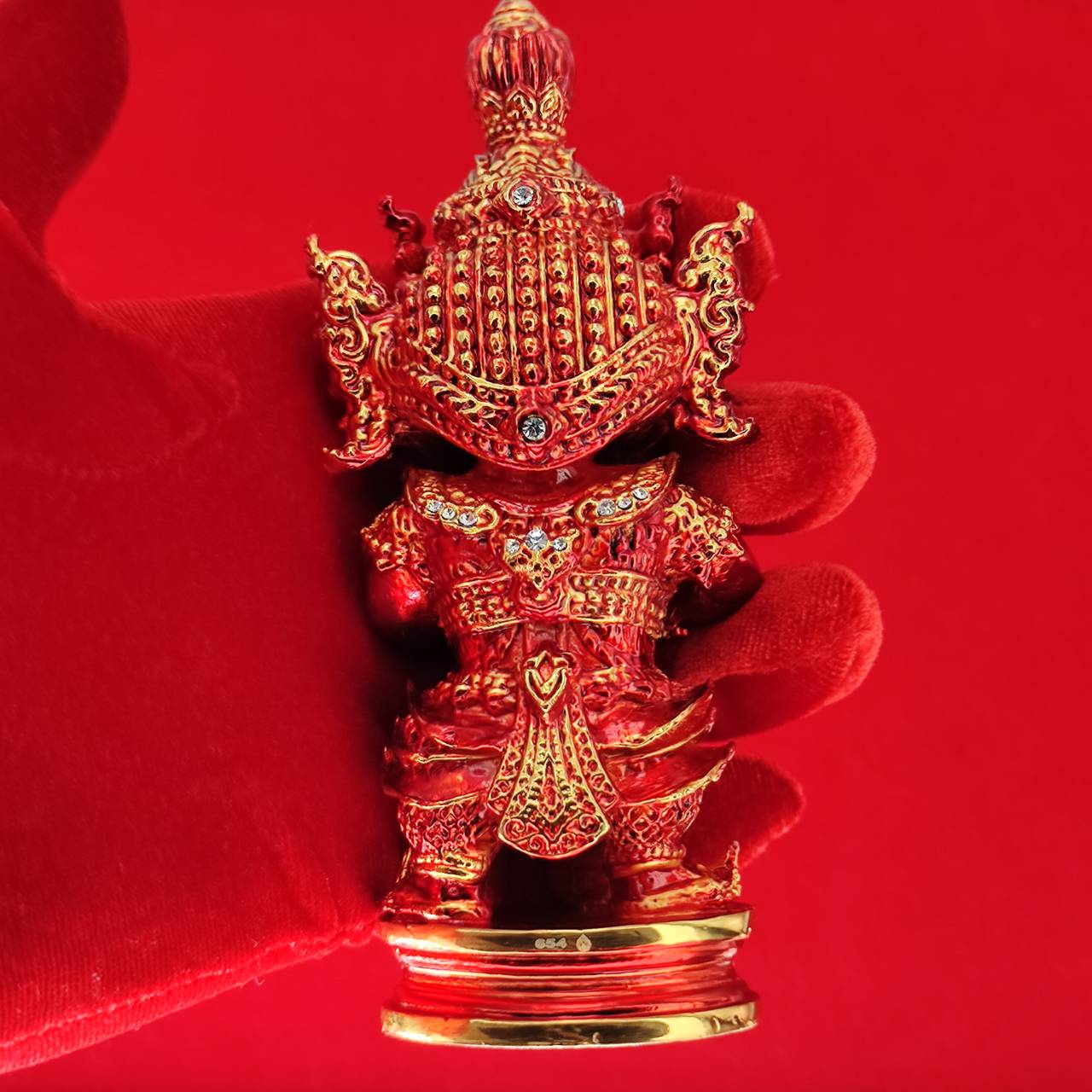Lord Vesuvanna lucky charm figurine in detailed red design with gold accents, held by a gloved hand against a red background