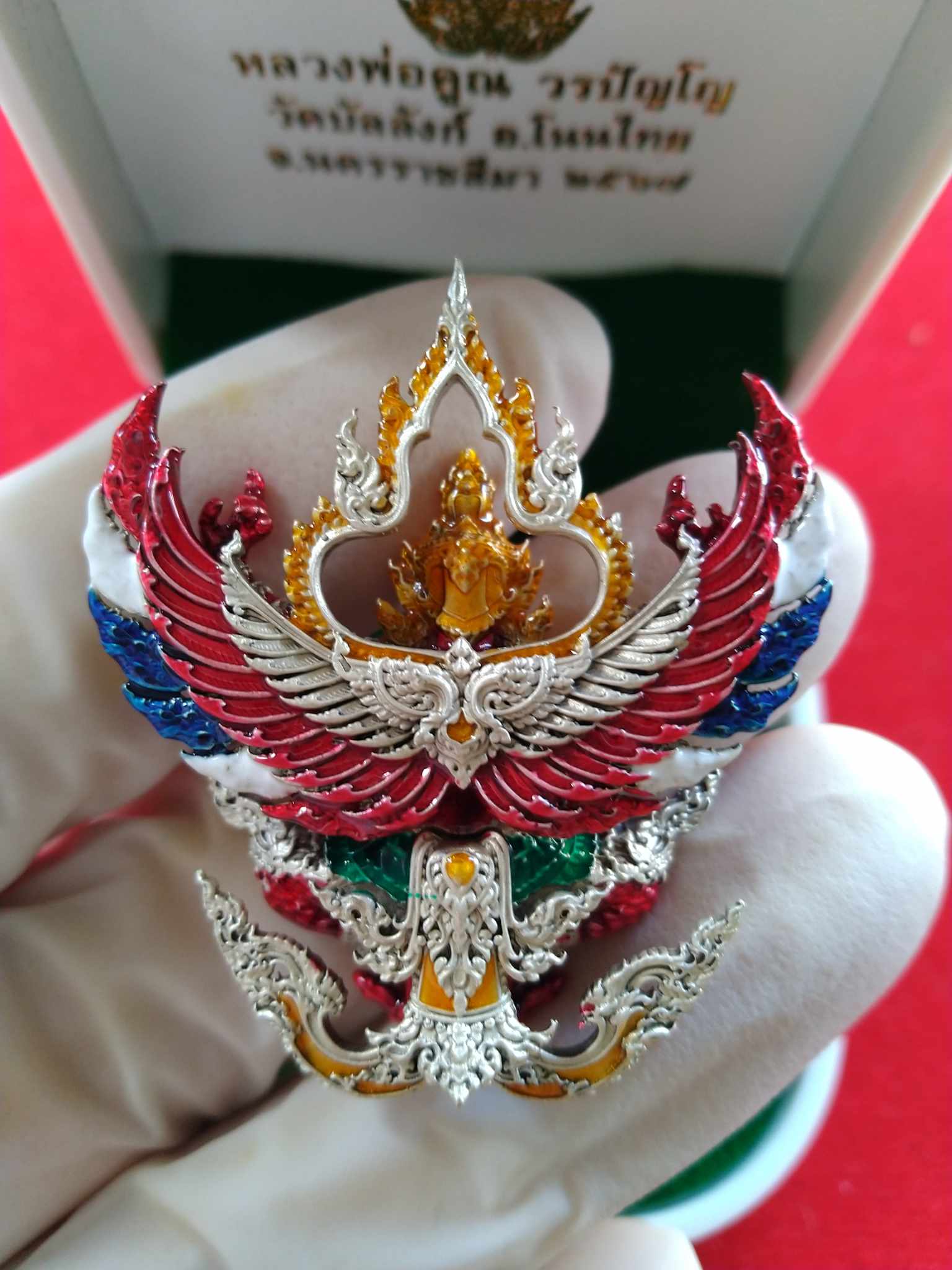Phaya Garuda amulet blessed by Luang Por Koon. Multicolor Thai Garuda pendant with silver gold enamel held in white gloved hand