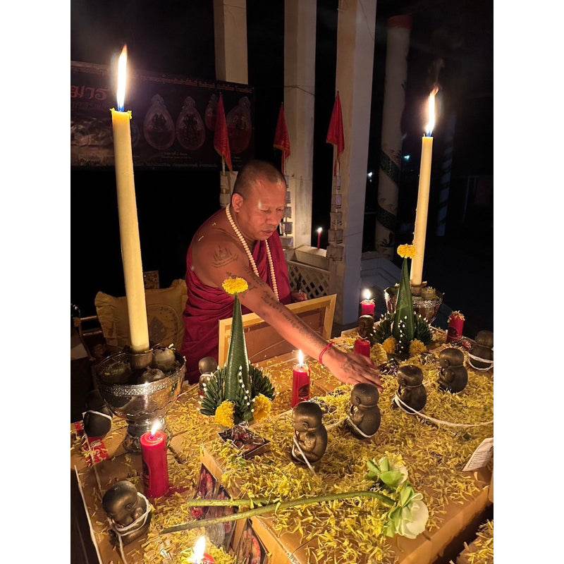 Monk performing candlelit altar ritual with small bronze figurines Guman Dood Rak on marigold petals