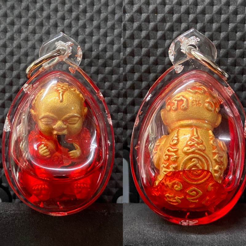 Guman Dood Rak Thai gold child amulet in red teardrop casing with engraved details and metal keyring
