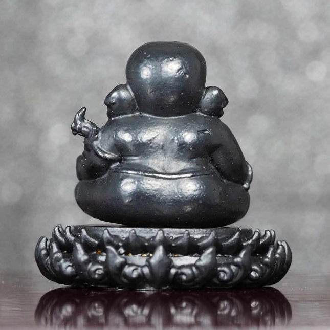 Black statue of Ganesha on lotus base for wealth with detailed carving on a reflective surface