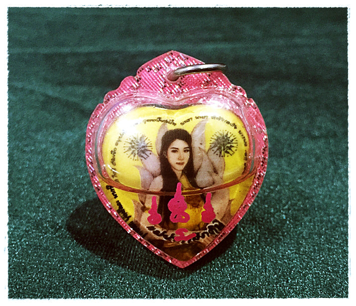 Pink heart pendant with female image and metal loop on green background, Thai Blessing Co Thai amulet for love and fortune