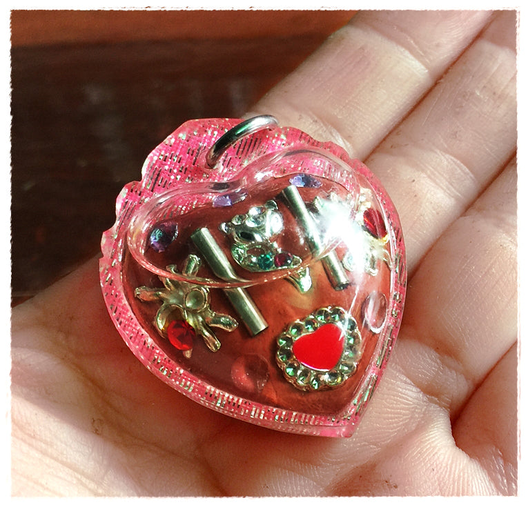 Hand holding pink heart pendant Thai amulet for love and fortune with gold charms and rhinestones