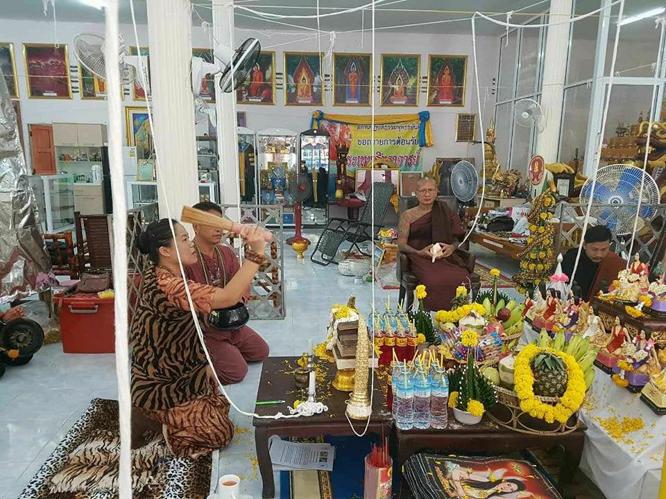 Temple blessing ceremony with monk devotees and altar offerings featuring Thai amulet for love and fortune