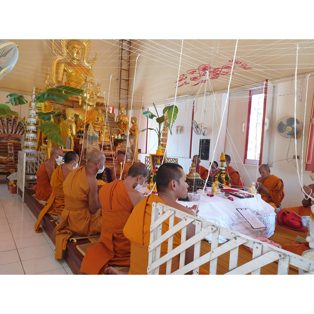 Thai monks in orange robes praying in temple surrounded by Buddha statues and religious items