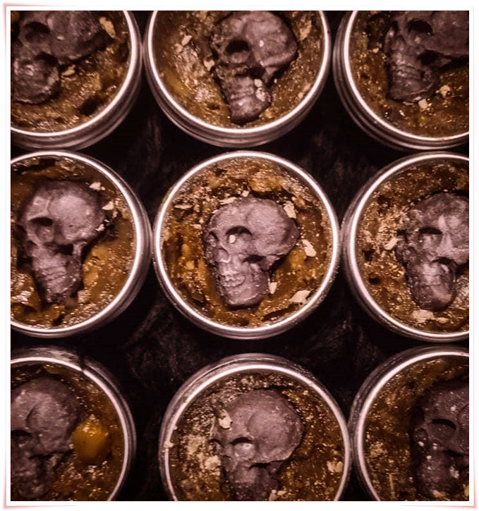 Thai Blessing Co tins of Namman Prai balm for spiritual power with small black skulls on herbal balm paste
