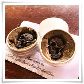Two open tins of dark herbal paste Namman Prai balm for spiritual power by Thai Blessing Co on paper
