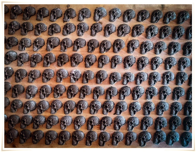 Rows of small black skulls containing Namman Prai balm for spiritual power by Thai Blessing Co on wooden tray