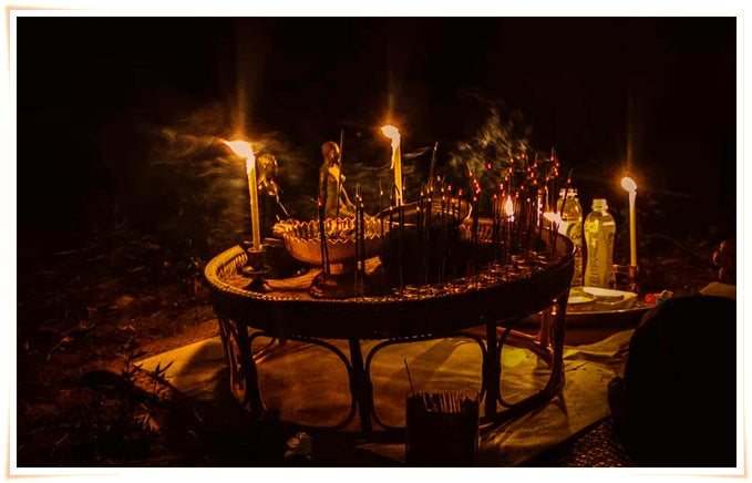 Namman Prai balm for spiritual power on a ritual altar with lit candles incense and offering bottles at night