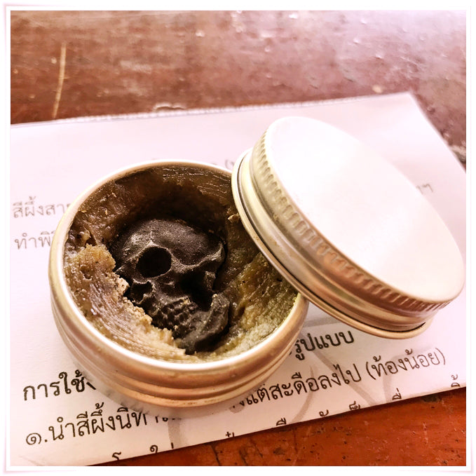 Thai Blessing Co Namman Prai balm for spiritual power in small metal tin with green balm and black skull charm on paper