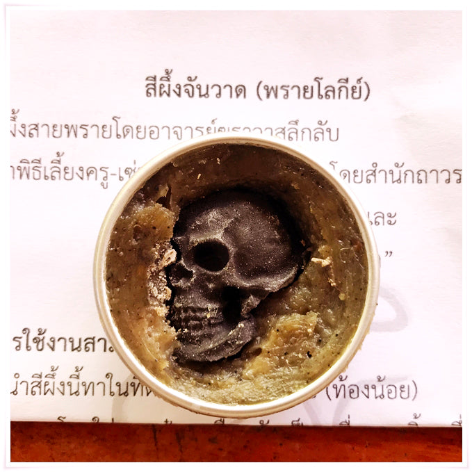 Thai Blessing Co tin of Namman Prai balm for spiritual power showing skull shaped black wax in green herbal balm