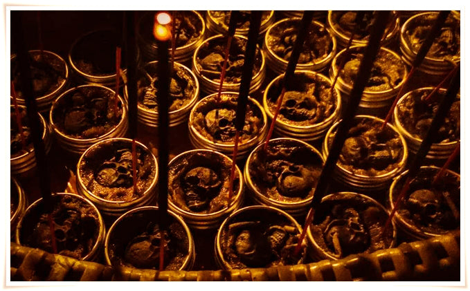 Multiple small brass tins of Namman Prai balm for spiritual power arranged with burning incense sticks