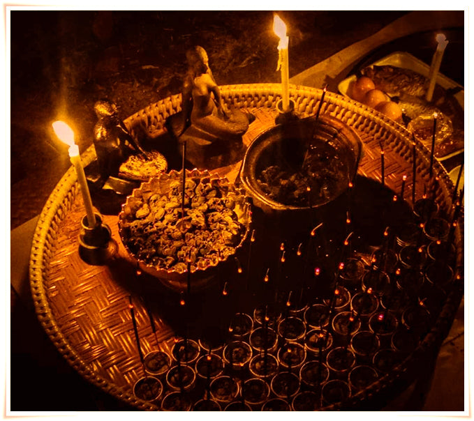 Namman Prai balm for spiritual power displayed on a woven offering tray with candles incense small votive cups and ritual figures